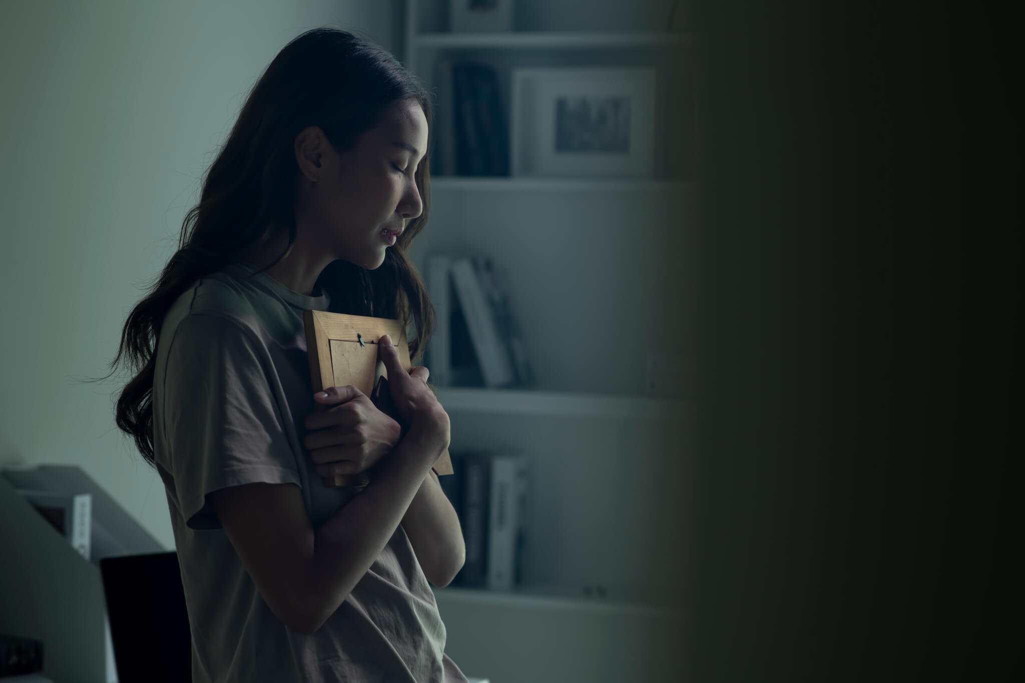 Asian women holding a photo frame of lost loved one and crying.